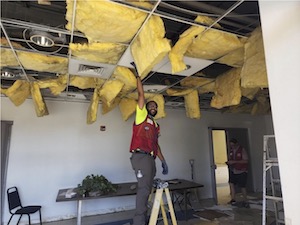 volunteer on ladder fixing ceiling