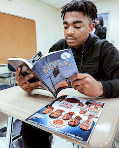 student sits at desk and reads magazine