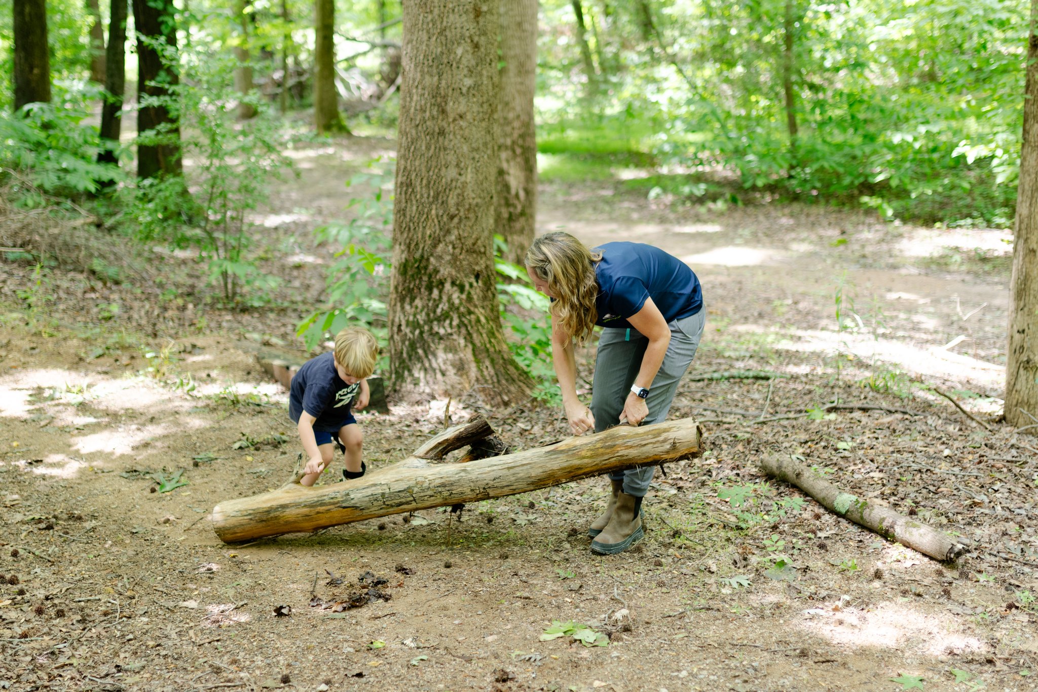 Physical therapist working with a child on lifting on a log in the woods