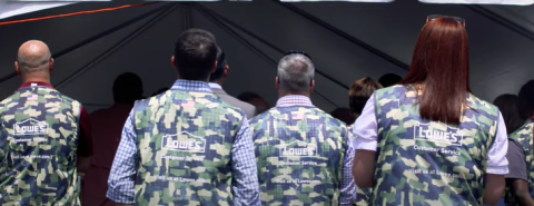 Lowe's workers in camo vests stand in line facing away from camera