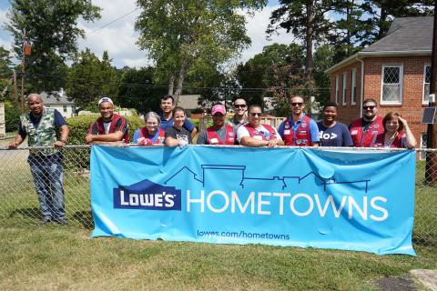 Lowe's team members post at fence behind hometowns sign