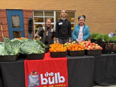 3 Volunteers stand behind a table full of fruits and vegetables 